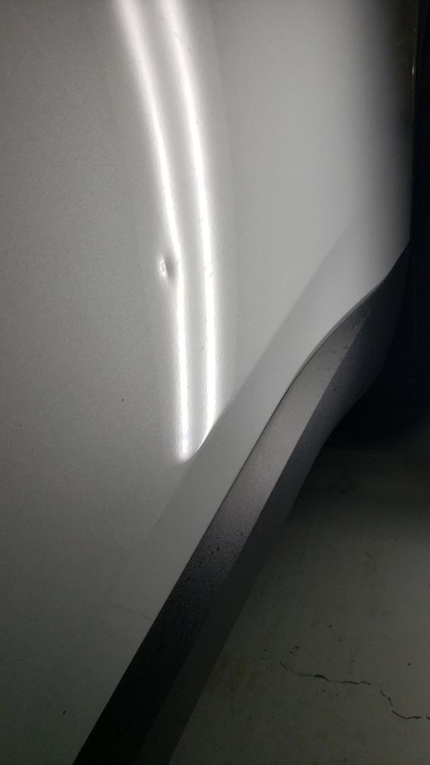 Car door ding close-up on a white panel before paintless repair