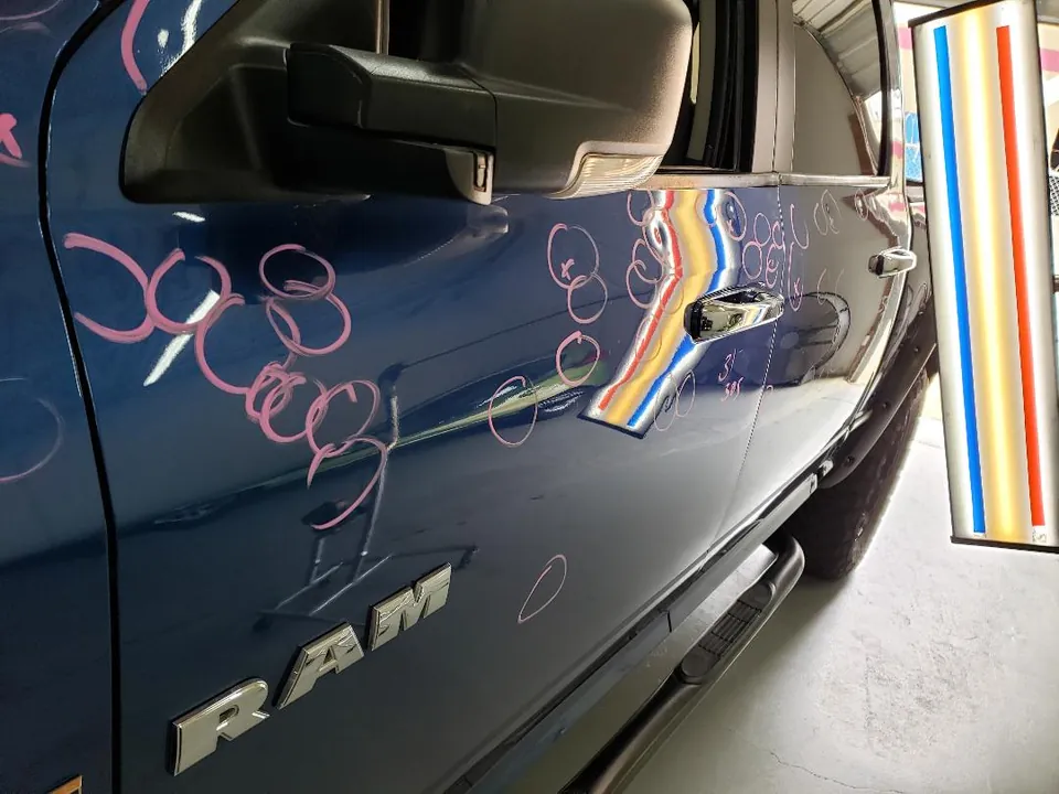 Blue RAM pickup with dents circled for paintless dent repair
