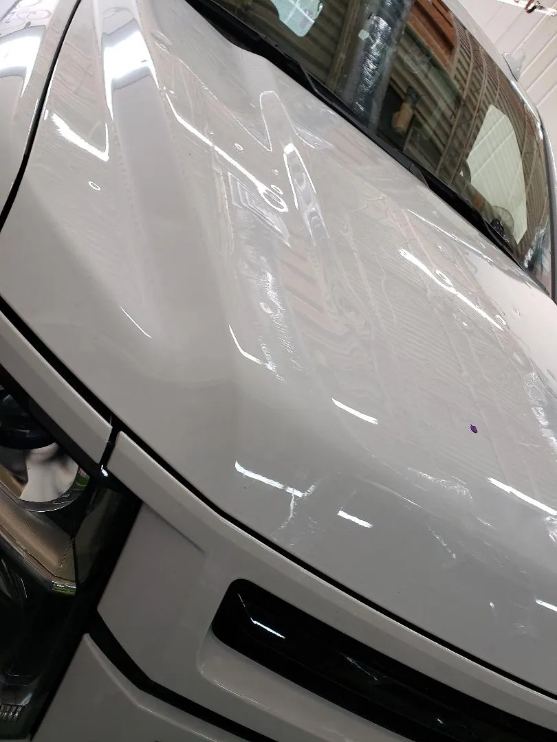 Hail dents across the hood of a white vehicle in a repair shop